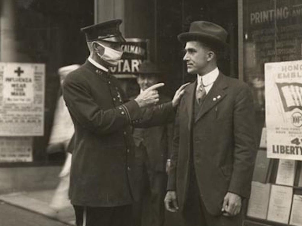 A policeman wearing a flu mask scolds a maskless man during the Spanish flu 
pandemic of 1918 (San Francisco).   |   Image: California State Library